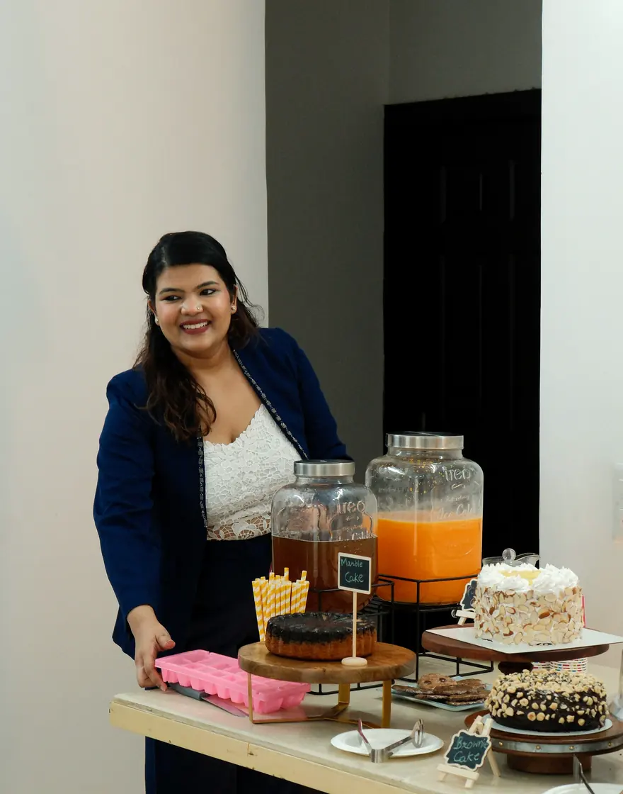 Sona Gupta smiling beside a table of cakes she has baked at the studio