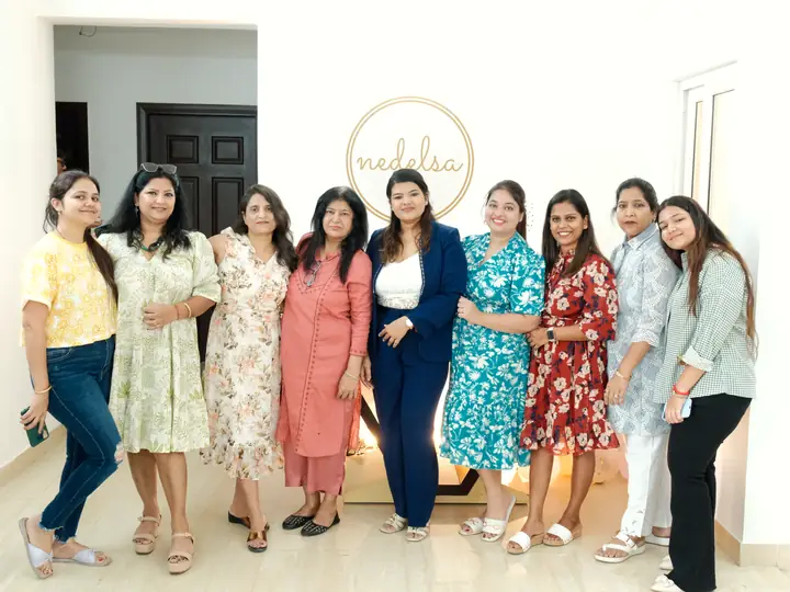 Nine women standing together under the Nedelsa mark at the studio