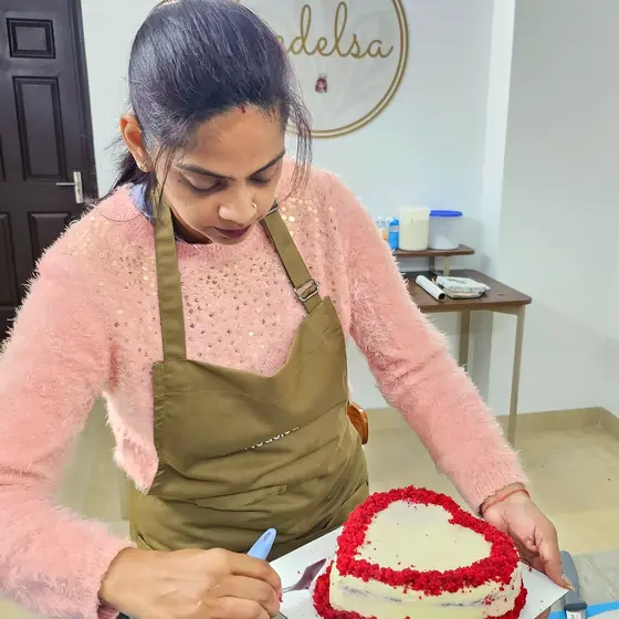 A student in a Nedelsa apron crumb-coating a red velvet heart cake with a palette knife