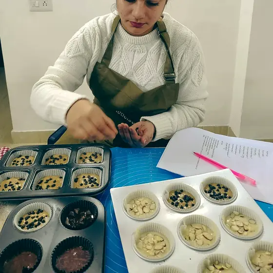 Overhead view of a student dropping chocolate chips into muffin liners beside two filled trays