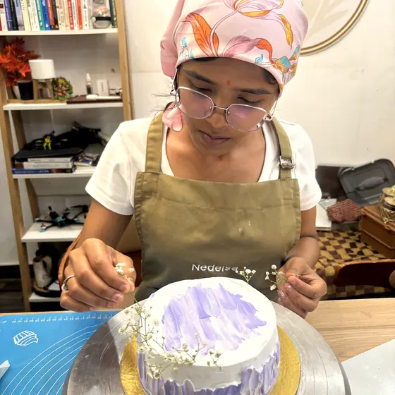 A student placing gypsophila onto a lilac brushstroke birthday cake