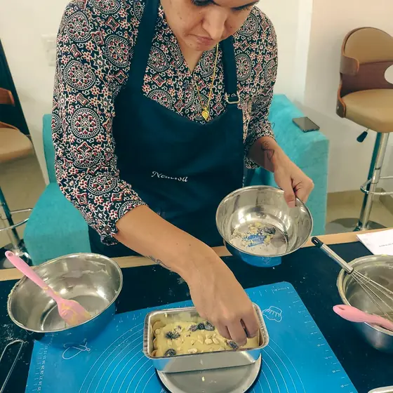 A student in a hairnet and Nedelsa apron placing berries and nuts onto a loaf tin