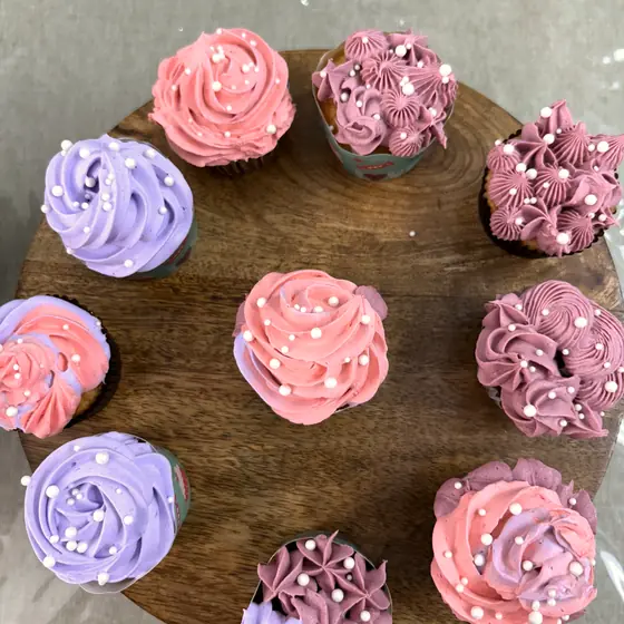 A wooden board of cupcakes piped in coral, lilac and mauve