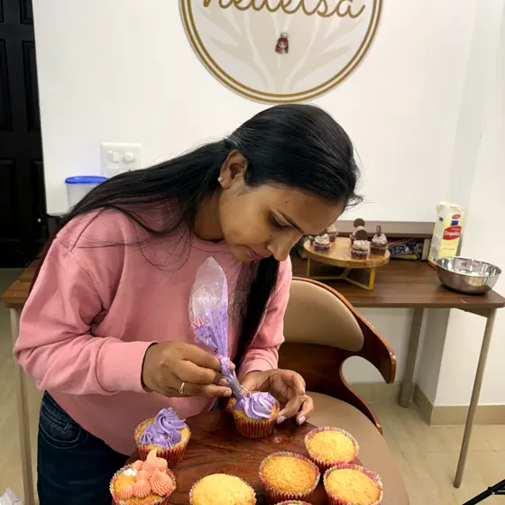 A student piping lilac buttercream onto a stand of vanilla cupcakes