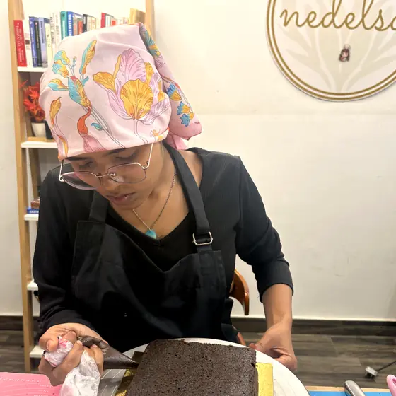 A student piping ganache onto a chocolate sheet cake at the studio bench